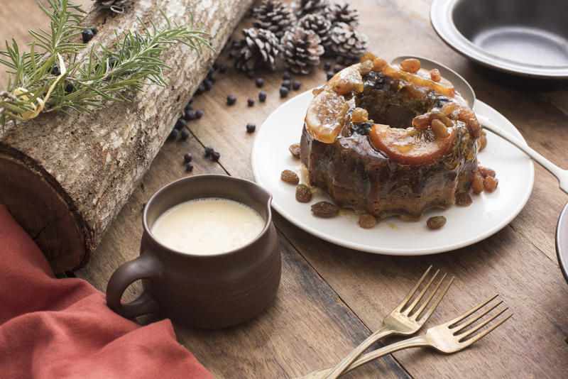 Tasty traditional Christmas plum pudding with fruit and brandy sauce on a decorated rustic table