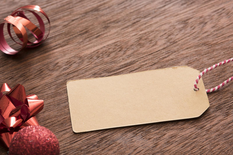 Blank brown gift tag with copy space for your holiday greeting lying on a wooden table with red Christmas decorations
