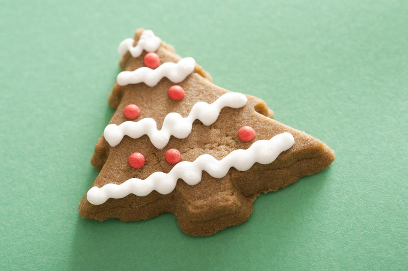 Christmas tree gingerbread cookie decorated with red and white icing on a green background with copy space