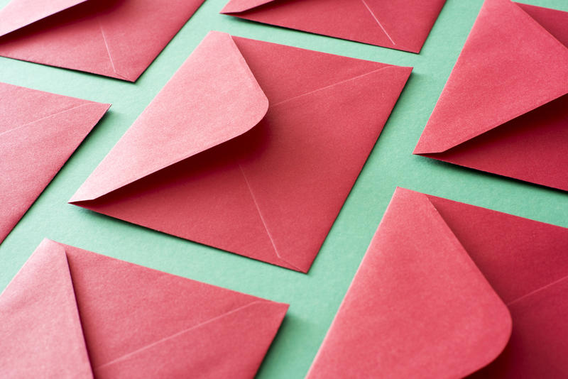 Festive red envelopes for Christmas or Valentines Day lying face down with open flpas on a textured green surface in a full frame diagonal view