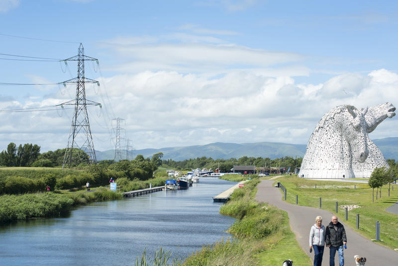 Tourists walking along path at the Kelpies landmark statue of two horse heads near canal in Scotland - not model released