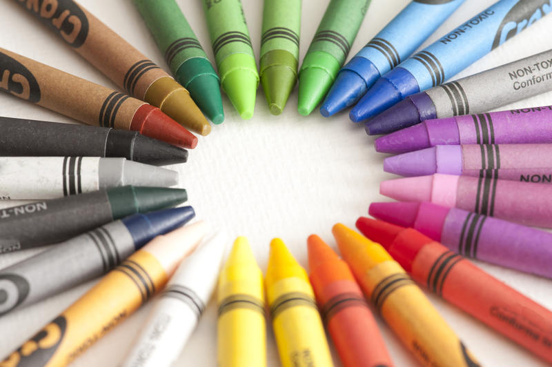 Frame of colorful wax crayons arranged in a radiating circle around central white copy space