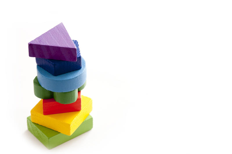 Still Life Stack of Colorful Wooden Blocks in Variety of Shapes Piled in Tower on White Background with Ample Copy Space