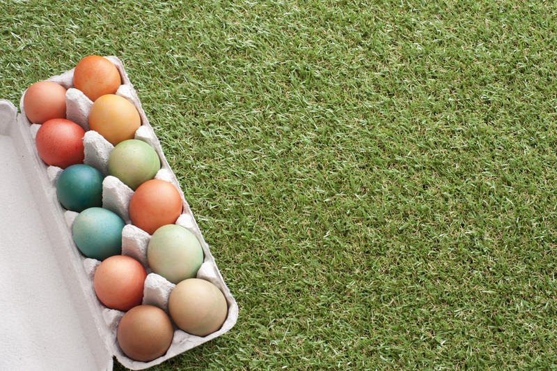 Box of dozen dyed Easter eggs of different colors on green grass loan background with copy space