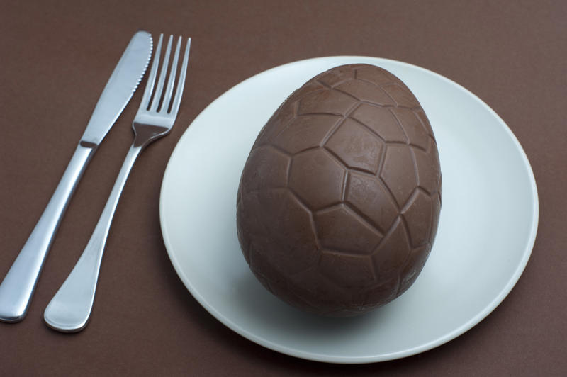 Serving of a chocolate Easter egg for dinner or dessert on a white plate with knife and fork in a conceptual image