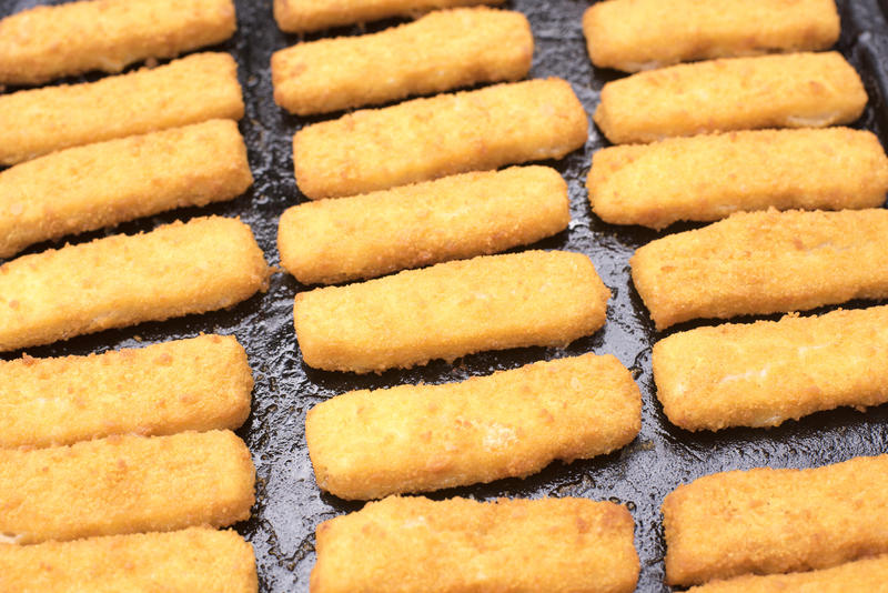 Greasy tray filled with baked and breaded fattening fish fingers sticks just baked in the oven