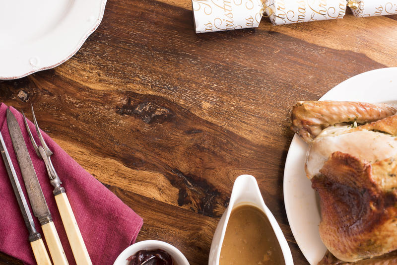 Christmas dinner frame composed of a roast turkey, utensils and sides with central copy space on a wooden dining table