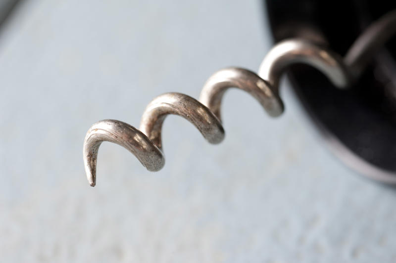 Close up on a steel corkscrew tip on a wine bottle opener over a textured white background with copy space