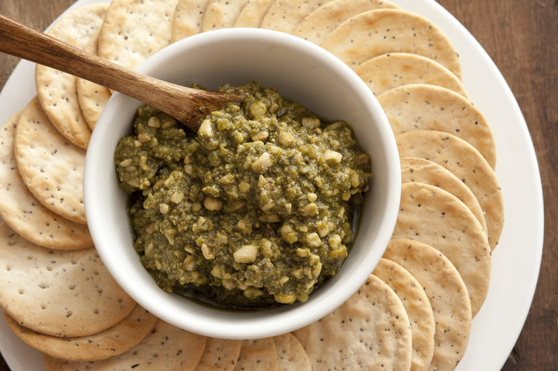 Above view on freshly prepared basil pesto cheese dip in bowl with round crackers on table