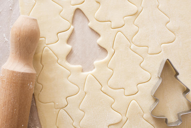 Baking homemade Christmas tree cookies with a close up view of uncooked dough with cut out shapes, a cookie cutter and rolling pin