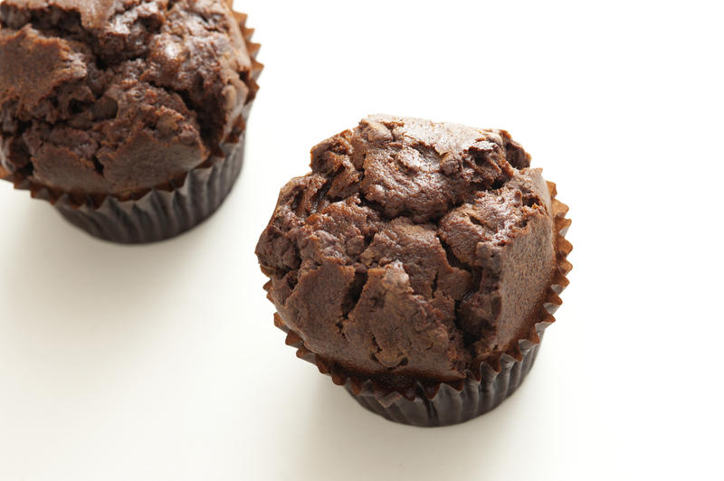 Two freshly baked dark chocolate muffins or cupcakes on a white background with copy space, high angle view