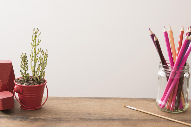 Designers desk or workspace with copy space with colored pencils in a glass jar, paintbrush and potted plant against a white wall