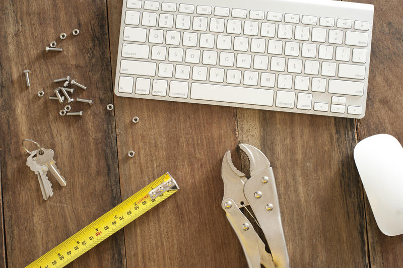 DIY or mechanical tools on a desk with a tape measure, mole grip, keys, nuts and bolts alongside a computer keyboard and mouse in a conceptual image