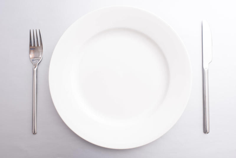 Clean empty white dinner plate with silver metal knife and fork in a simple place setting ready to serve food