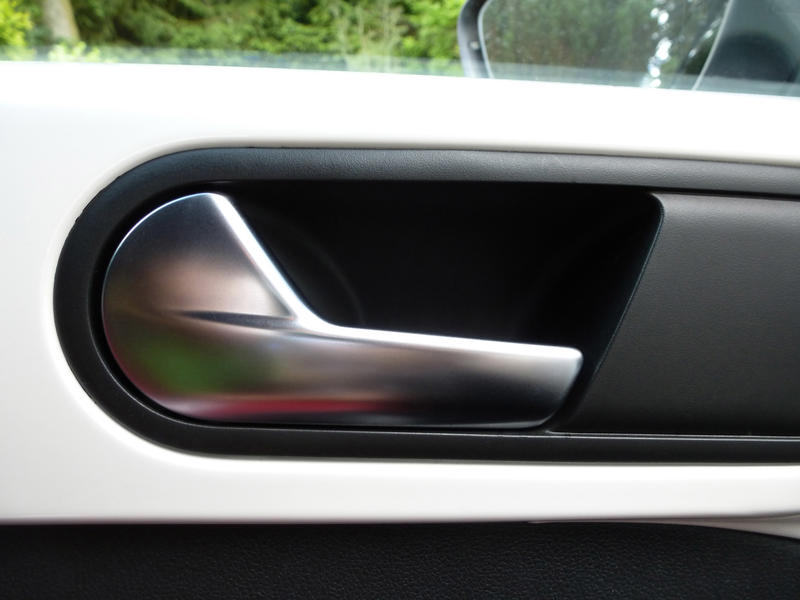 Metal car door handle in black trim on a white car parked in front of greenery, close up interior view