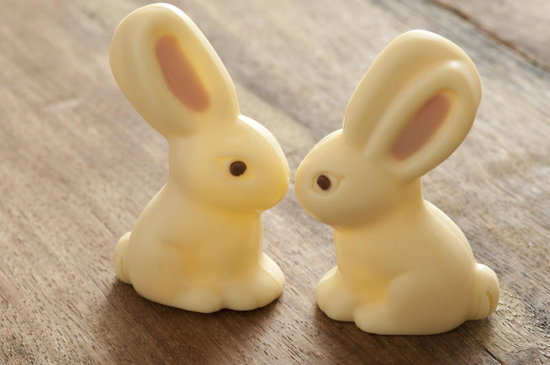 Close-up of two Easter bunny candies of white chocolate sitting on wooden table close, as if kissing