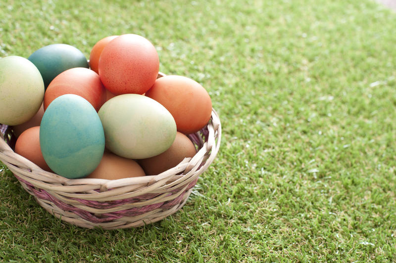 Rustic woven wicker basket of traditional dyed Easter Eggs on a green lawn with copy space alongside