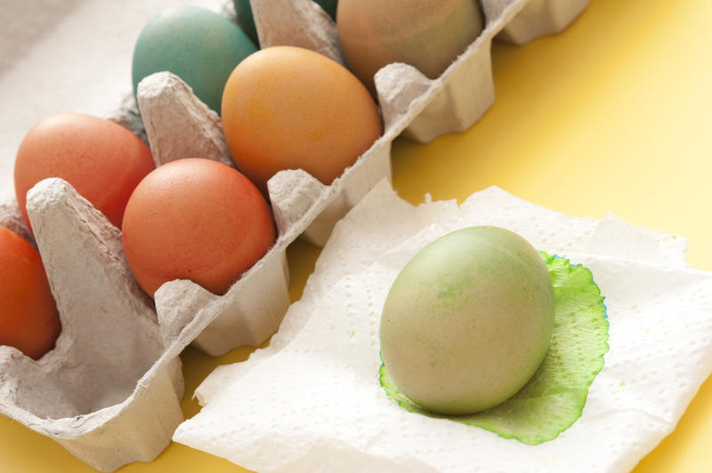 Dyeing colorful homemade boiled Easter eggs in a country tradition with a cardboard box full alongside a single green egg drying on a paper napkin