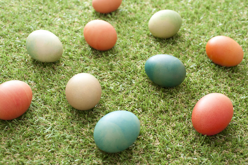 Scattered homemade dyed Easter eggs in pretty pastel colors on neat green spring grass viewed at an oblique angle for a holiday background