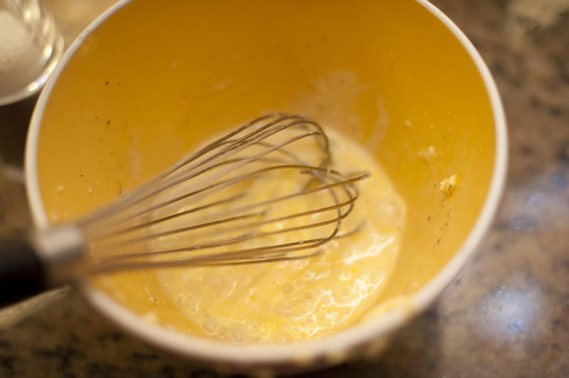 Overhead view of eggs in mixing bowl with whisk having been whipped and having the same yellow color as the bowl
