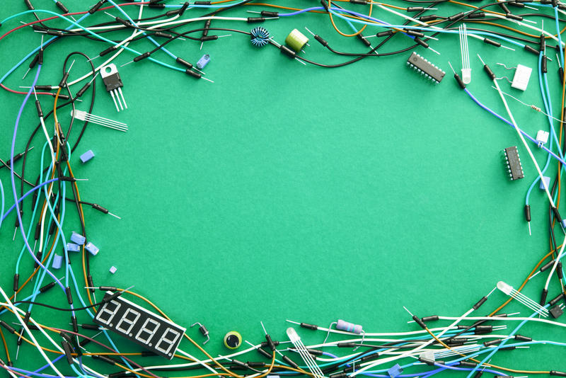 Colorful plastic coated electronic wires and connectors forming a frame on a green background with central copy space