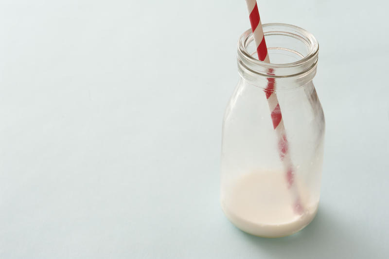 Lone glass bottle nearly emptied of white milk and having a single striped straw