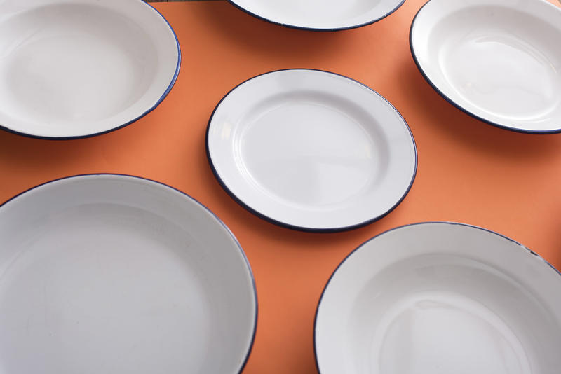 Plain white clean empty enamel plates on an orange background in a close up view and focus to a centre plate