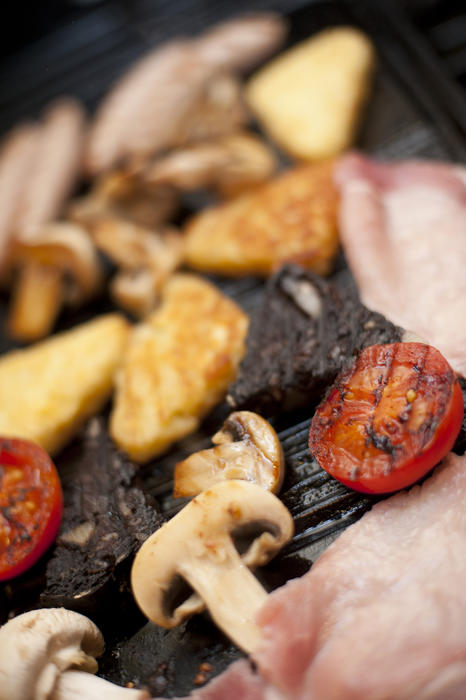 Close up view of grilled mushrooms and tomato besides charred meat and some raw pieces