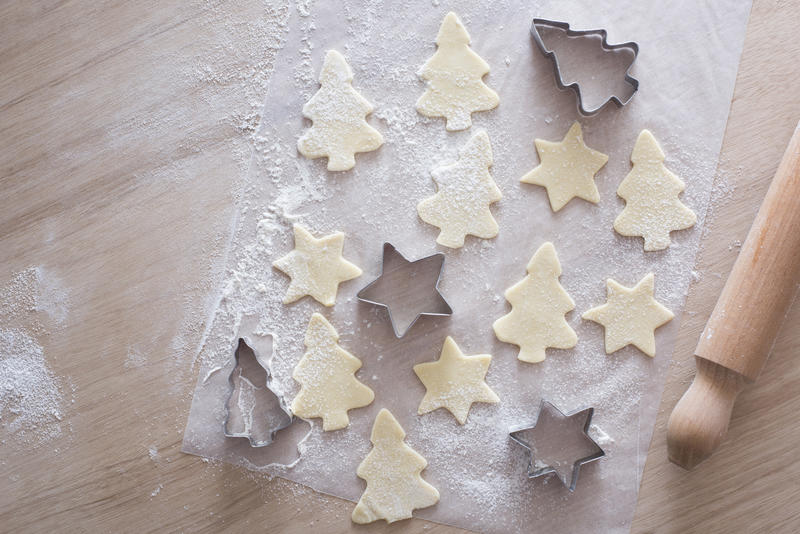 Overhead view of unbaked tree and star shaped cookies beside tin cutters and rolling pin