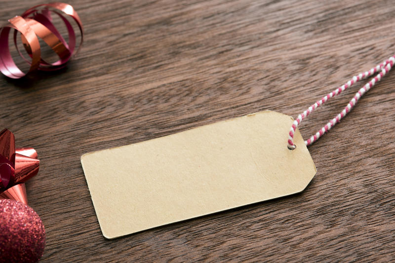 Blank Christmas gift tag with red themed decorations forming a side border on wood with copy space for your greeting or message