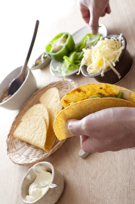 Man filling a taco with sour cream or mayonnaise, fresh green peppers and cheese using his fingers to pick up the ingredients
