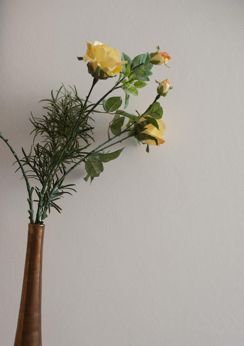 Delicate arrangement of long stemmed yellow roses in a vase with green foliage over a grey background with copyspace
