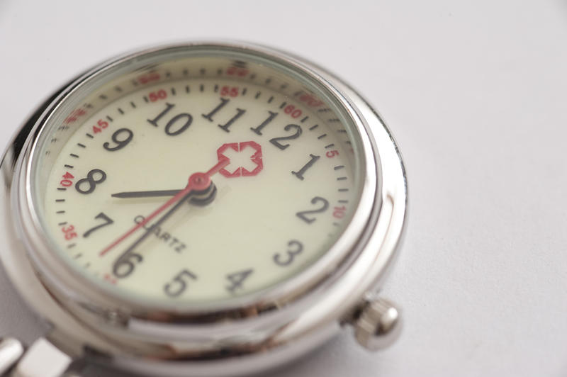 Close up on the round silver metal dial of a nurses watch with a red cross on the face in a time keeping and precision concept