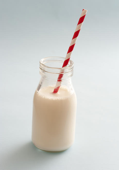 Small glass bottle full of fresh creamy healthy milk with a straw over a grey background in a healthy diet for kids concept