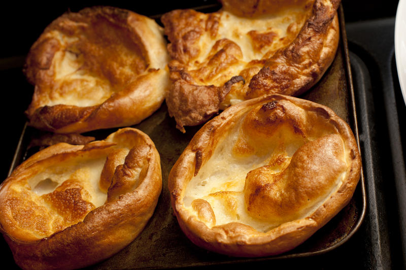 Four fresh Yorkshire pudding cups browned and bubbled in muffin tin on stove top