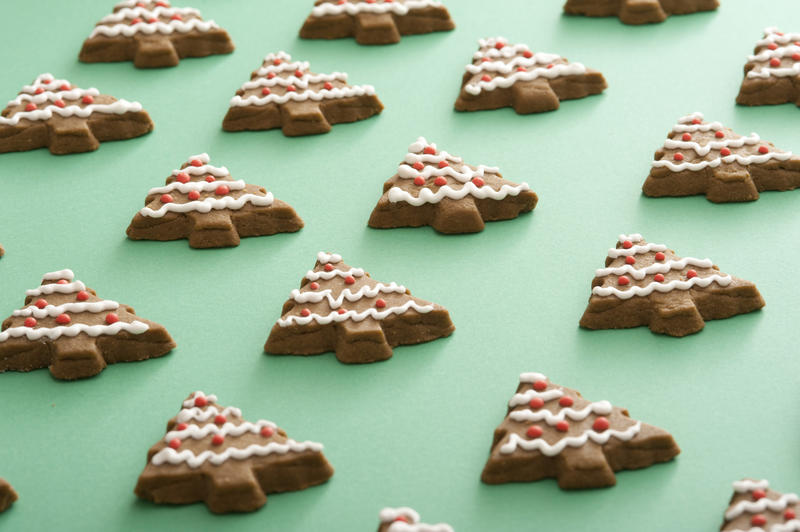 Green cookie sheet laid with rows of tree shaped goodies with white and red frosting