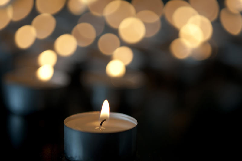 Close-up image of little candle tealight burning in the dark with many glimmering candles blurred in bokeh effect background
