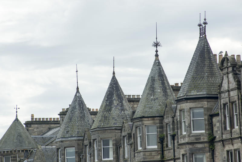 Historic stone architecture in St Andrews, Scotland with a row of octagonal turrets on a building facade against a grey cloudy sky
