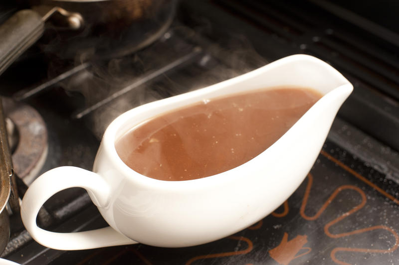 Gravy boat filled with rich hot gravy made from meat drippings and stock standing on a warming plate