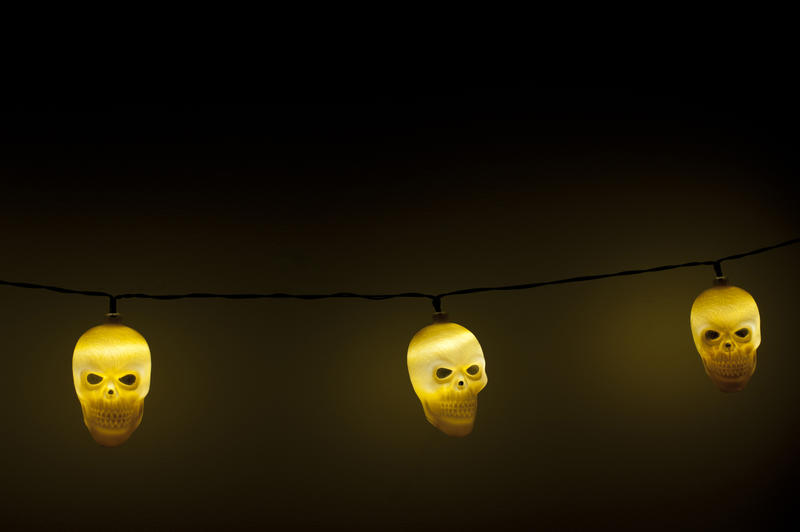 Close Up of String Glowing Halloween Skull Lights Suspended in Eerie Dark Room Against Plain Wall with Copy Space