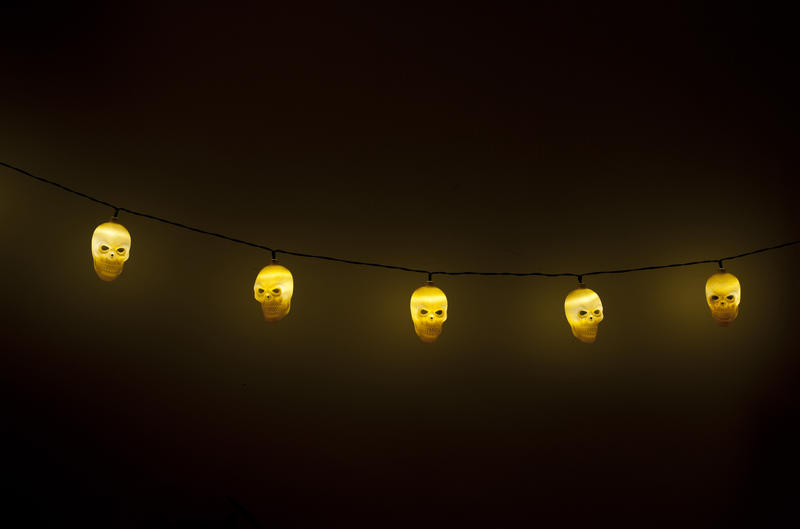 String of ghostly glowing yellow Halloween skull lights against a black background with copy space