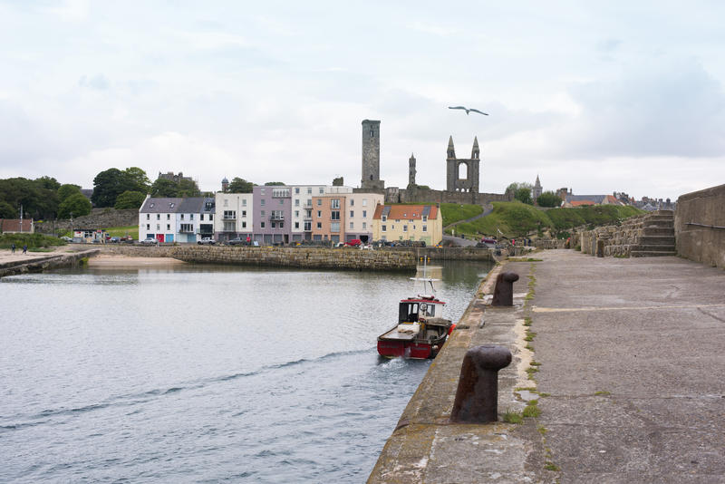 Single little boat at large pier with old Saint Andrews Cathedral and houses in background