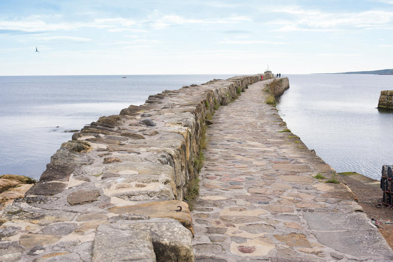 View along the receding length of the stone sea wall or pier at St Andrews harbour, Scotland on a calm day with cloud cover