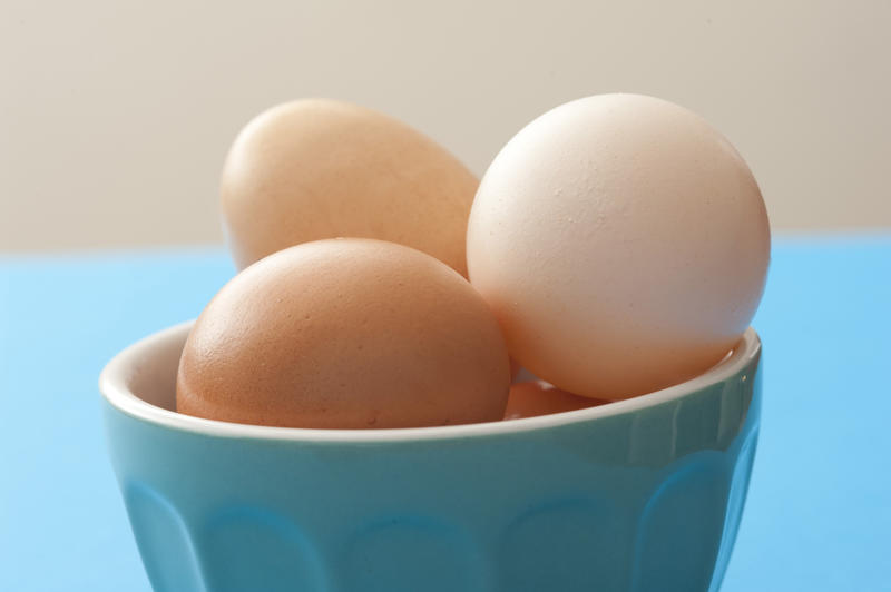 Fresh whole raw brown and white hens eggs in a blue ceramic bowl on a blue kitchen table in a close up view