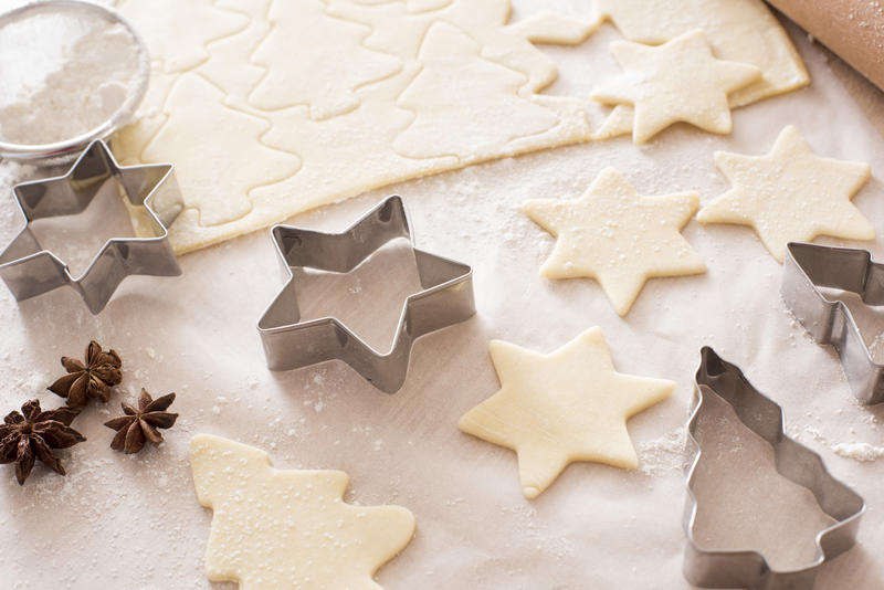Making star and tree-shaped Christmas cookies at home with meal cookie cutters and star anise spice with cut out uncooked pastry on floured oven paper