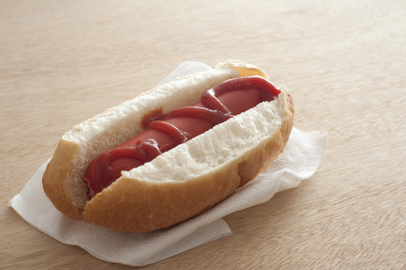 Single ready to eat hot dog covered in ketchup on napkin over table with copy space