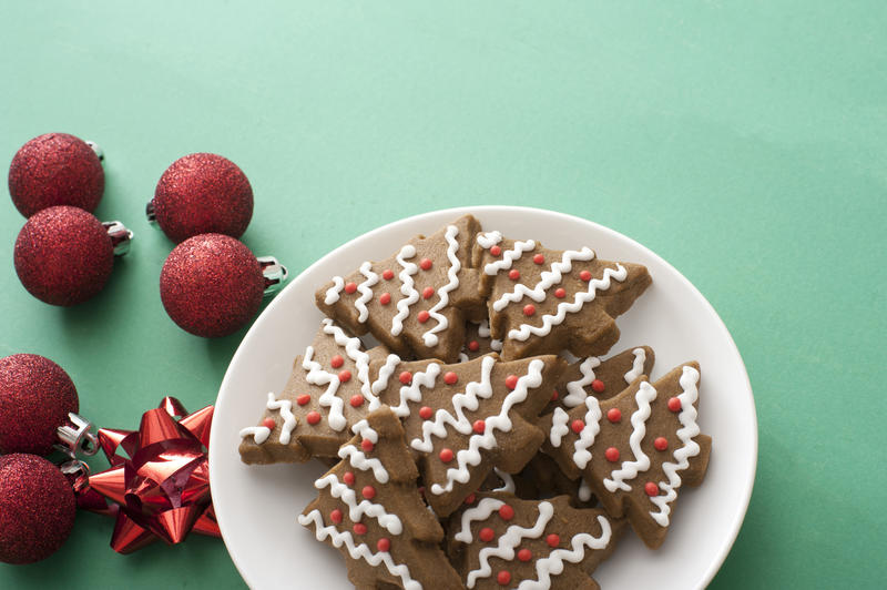 Iced gingerbread Xmas tree cookies served on a plate alongside festive red Christmas baubles and bows on green with copy space for your greeting