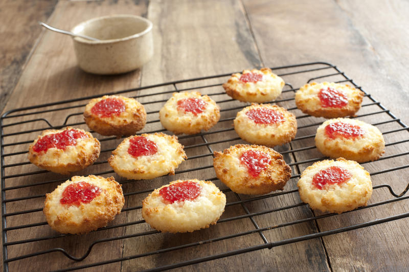 Batch of delicious jam drop biscuits filled with strawberry jam cooling on a wire rack in the kitchen on a wooden counter