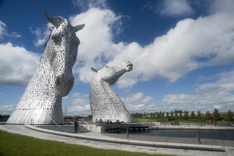 Canal in front of two large horse head Kelpies statues under beautiful blue sky with white fluffy clouds