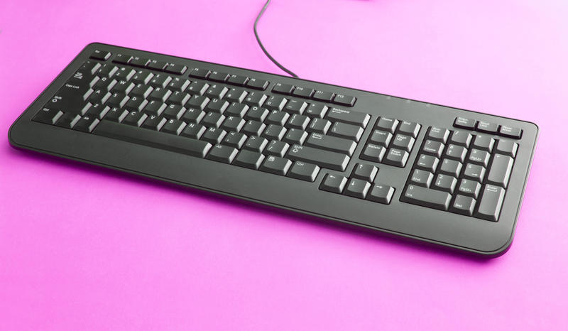 Black wired computer keyboard on a bright pink background with copy space, high angle view